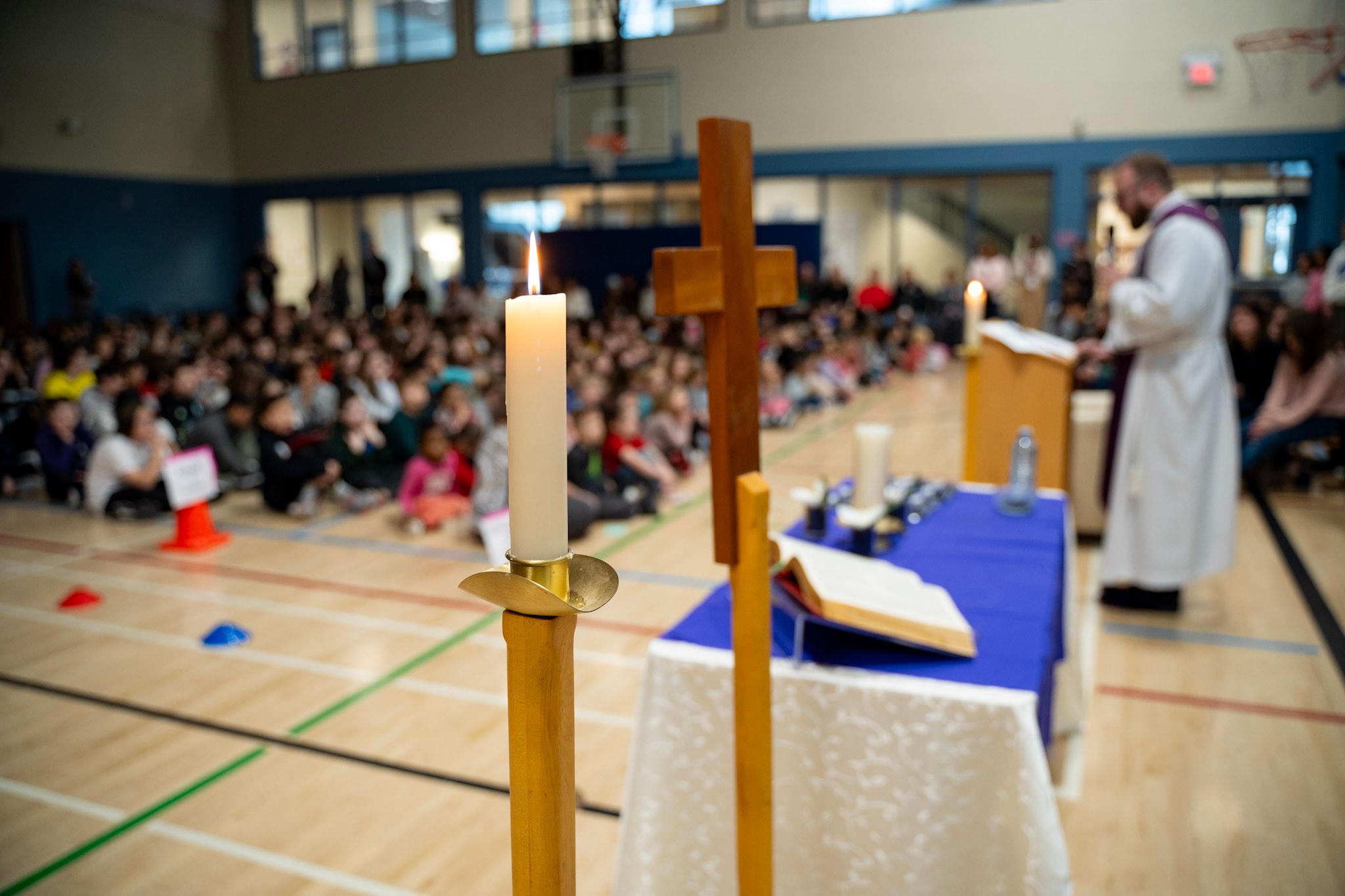 View of a gynamisum where students and a priest are celebrating mass, candle and cross in the foreground.